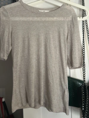 Ljusgrå kortärmad t-shirt från H&M - Säljer en enkel och stilren ljusgrå t-shirt från H&M. T-shirten har rund hals och korta ärmar, tillverkad i mjuk bomull som är skön mot huden. Passformen är normal och färgen är diskret melerad ljusgrå, perfekt för en chill och clean look.