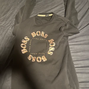 Svart t-shirt från Hugo Boss med logga - Säljer en svart t-shirt från Hugo Boss med rund hals och tryckt BOSS-logga i cirkel på bröstet. T-shirten har en klassisk passform och är perfekt för en stilren look.