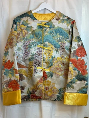 Silk jacket  - Beautiful padded jacket made from 100% genuine mulberry silk. The outer fabric features an elegant oriental floral pattern with a subtle sheen, while the lightly padded lining provides warmth without bulk.  ✨ Highlights: • 100% mulberry silk outer layer • Lightly padded – warm yet lightweight • Classic straight fit with decorative buttons • Unique, timeless piece – not mass-produced  📏 Measurements (laid flat): Bust: 106 cm Shoulder: 41 cm Length: 62 cm   💛 Perfect for those who love silk, vinta