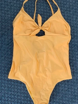 Gul body med knyt och cut-out - Snygg gul body med smala axelband och ett knyt framtill som ger en cool cut-out detalj under bysten. Modellen är enkel men har en trendig touch med knytet och den ljusa färgen. Perfekt för en varm dag.