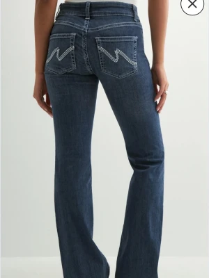 Bootcut jeans från Nelly med broderad ficka - Snygga mörkblå bootcut jeans från Nelly med vit broderad detalj på bakfickorna. Använd få gånger pga längd 