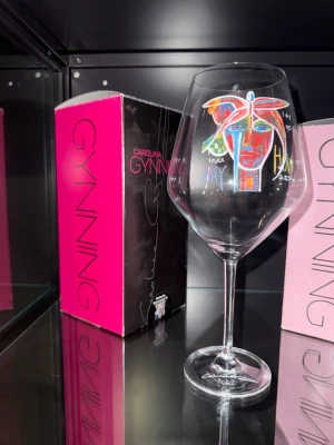Carolina Gynning glas - Carolina Gynning vinglas med färgstarkt, konstnärligt ansikte tryckt framtill. Designen har inslag av blått, rött, gult och grönt i ett grafiskt mönster. 1st rödvinsglas 2st vitvin/rosé glas