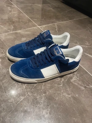 Valentino flycrews marinblå sneakers - Snygga sneakers från Valentino Garavani i marinblå mocka och vitt skinn. Skorna har snörning, rund tå och platt sula med coola nitar baktill. Perfekt för dig som gillar exklusiva märken och vill sticka ut med stilrena detaljer.