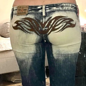 Crazy age jeans med trampstamp - Jag gjorde ett collage för att få plats med alla bilder, så jag ber om ursäkt om de är otydliga 😅Alla defekter syns på bilderna. Fläcken på byxorna är liten och svag. Defekter: fläck, lagningar och benöppningar. Byxorna sitter som på bilden trots lagningar och benöppning. För tillfället är jag tyvärr inte öppen för prisförhandlingar, men jag kommer nog att ändra mig om några veckor eller kanske 2-3 månader.   Innerben: 81 cm Midja: 41 cm Midjehöjd/rise: 17 cm Lår: 24 cm Benöppning: 27 cm