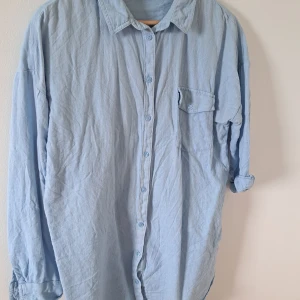 Ljusblå skjorta från KappAhl - Ljusblå skjortklänning från KappAhl i bomull med klassisk krage, bröstficka med knapp och långa ärmar. Skjortan har en avslappnad passform och stängs med knappar framtill. Perfekt för en chill och stilren look.