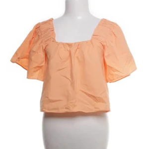 Persikofärgad blus med puffärm - Säljer en söt persikofärgad blus med bred fyrkantig ringning och voluminösa puffärmar. Blusen har rynkade detaljer vid axlarna och är croppad i modellen. Perfekt för dig som gillar ljusa färger och en luftig stil.