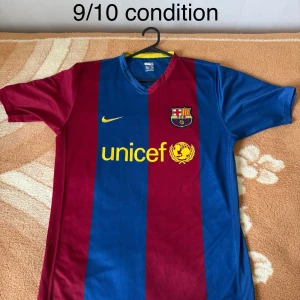 FC Barcelona Nike fotbollströja M - Klassisk FC Barcelona fotbollströja från Nike i storlek M. Tröjan har breda blå och vinröda ränder, klubbmärke på bröstet och gul Nike-logga samt UNICEF-tryck. Tillverkad i lätt och ventilerande polyester, perfekt för match eller träning.