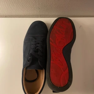 Christian Louboutin svarta sneakers 39 - Säljer ett par svarta sneakers från Christian Louboutin i mocka med klassisk röd sula och snygg snörning. Skorna har rund tå och innersula med Louboutin-logga. Perfekta för dig som vill sticka ut med exklusiva detaljer. Vet inte ifall dom är äkta men dom är jävligt snygga, PRIS KAN DISKUTERAS