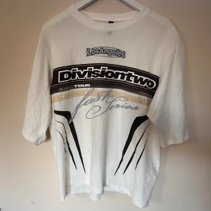 Vit t-shirt Divisiontwo H&M Divided S - Vit t-shirt från H&M Divided i storlek S med tryck framtill: 'Los Angeles', 'Divisiontwo', 'fast series' och grafiska detaljer i svart, grått och beige. Klassisk passform, rund hals och korta ärmar. Tillverkad i mjuk bomull.