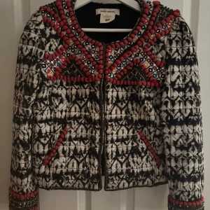 Broderad jacka Isabel Marant x H&M - Unik och broderad jacka från Isabel Marant x H&M med svartvitt rutigt mönster och röda pärldetaljer. Jackan har quiltad struktur, lång ärm och coola broderier vid axlar och fickor. Perfekt statement-plagg för dig som gillar att sticka ut.