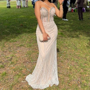 Champagnefärgad glittrig balklänning/ bröllopsklänning fest klänning  - Säljer en elegant långklänning i champagnefärg med glittriga pärldetaljer och transparent mesh upptill. Klänningen har en unik asymmetrisk axelrem och figurnära passform som framhäver siluetten. Perfekt för bal eller student! Materialet är troligtvis polyester med paljetter.