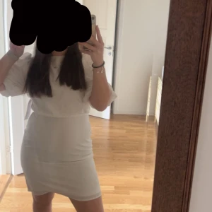 Vit kortklänning med puffärmar - Supersöt vit kortklänning  med puffiga kortärmar och rund hals. Klänningen har en snygg knytning i ryggen och är figurnära i midjan. Perfekt för dig som gillar stilrent. Köpte för att ha på studenten, men ångrade mig och kom aldrig till användning. Köpte den för 300kr på Black Friday förra året. Skulle säga att den är liten i storleken då den passar mig som vanligtvis har S/36. 