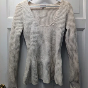 Ljusbeige ribbad stickad tröja - Säljer en beige stickad tröja med ribbad struktur och bred, rundad halsringning. Tröjan har långärmade ärmar och en lätt utsvängd nederdel som ger en snygg siluett. Perfekt för dig som gillar mjuka och mysiga plagg med enkel design.