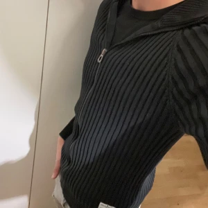 Svart cardigan - Säljer en svart cardigan från Jack & Jones med ribbad struktur och dragkedja framtill. Perfekt för dig som gillar stilren och enkel design. Passar dig som vill ha en bekväm och snygg tröja med lite edge.