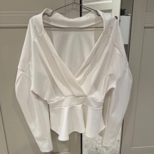 Peplum top med volang - Säljer en vit peplum med v-ringad hals och volang nedtill. Toppen har långa ärmar och är tillverkad i ett mjukt, slätt material som ger en clean och fräsch look. Perfekt för dig som gillar stilrena och feminina detaljer.