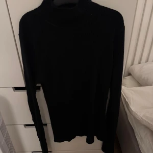 Svart ribbad polotröja KappAhl M - Svart polotröja från KappAhl i storlek M. Tröjan är ribbad och har lång ärm samt hög krage som ger en clean och stilren look. Perfekt att styla med jeans eller kjol för en chill vibe. Materialet är mjukt och stretchigt för skön passform.