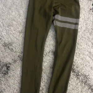 Olivgröna leggings - Snygga olivgröna leggings med två reflekterande ränder på ena låret. Perfekta för träning eller chill. Stretchigt material som sitter tajt och bekvämt.