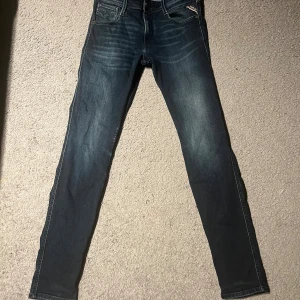 Replay jeans i mörkblå denim, 28/32 - Snygga Replay jeans i mörkblå tvätt med klassiska fem fickor och diskreta slitningar framtill. Modellen har smal passform och raka ben. Jeansen är tillverkade i bomull och har detaljerade sömmar samt läderpatch bak i midjan.