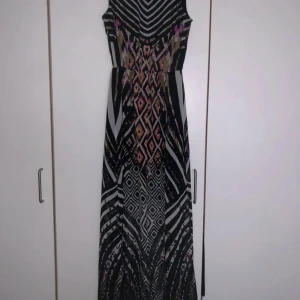 Mönstrad långklänning från ONLY - Snygg långklänning från ONLY med grafiskt mönster i svart, vitt, beige och inslag av rosa och lila. Klänningen är ärmlös och har en figurnära passform upptill med markerad midja. Materialet är lätt och flowy, perfekt för dig som gillar unika prints.