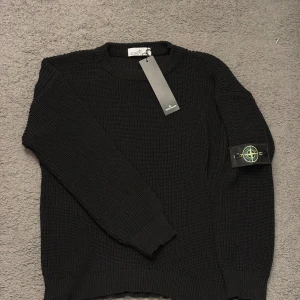 Stone Island tröja - Svart stickad tröja från Stone Island med klassisk rund hals och ribbade muddar. Ikonisk logotyp-patch på vänster ärm ger en clean och exklusiv vibe. Perfekt för dig som gillar streetwear och vill ha något som sticker ut.