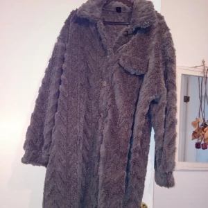 Grå teddyjacka med krage - Säljer en fluffig grå teddyjacka med bred krage och knappstängning. Jackan har en stor ficka på bröstet och är långärmad. Perfekt för dig som vill ha en mysig och trendig look under kyliga dagar. Ny endast tvättad