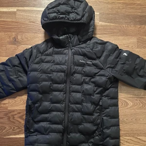 Svart Peak Performance pufferjacka 160 - Svart pufferjacka från Peak Performance med huva och två sidofickor med dragkedja. Jackan har quiltad design och logga på bröstet samt ärmen. Perfekt för kalla dagar och har en stilren look som funkar till det mesta. Köpt på Kidsbrandstore nypris ca 2000kr! Pris går att diskutera👌