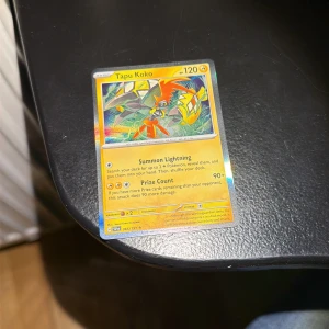 Tapu Koko Pokémonkort (065/191, Holo) - Tapu Koko holofoil-kort från Sword & Shield-serien, nr 065/191. Kortet är i gott skick med tydliga färger och glans. Perfekt för samlare eller spelare som vill stärka sin el-lek. Inga synliga större skador eller slitage på fram- eller baksida.