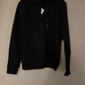 Svart hoodie med tryck - Svart hoodie med stor vit logga på ryggen och mindre logga framtill. Tröjan har huva med snörning och en ficka framtill. Mjuk bomullskänsla och långärmad modell.