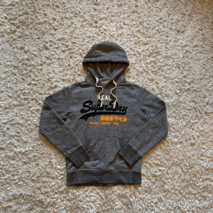 Grå hoodie från superdry - Snygg grå hoodie från superdry. Toppskick utan defekter. Storlek S, tveka inte på o skriva vid fler frågor!