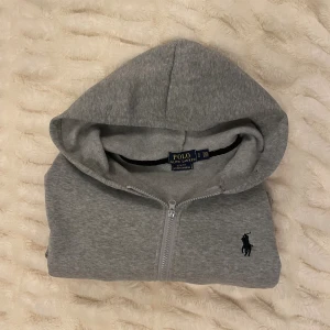 Grå hoodie från Polo Ralph Lauren - Snygg grå hoodie från Polo Ralph Lauren med dragkedja. Perfekt för en mer avslappnad look                                                       Nypris runt 2000kr