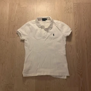 Vit pikétröja Ralph Lauren M - Vit pikétröja från Ralph Lauren i modellen The Skinny Polo dam modell. Klassisk design med korta ärmar, krage och liten broderad logga på bröstet. Tröjan har en slim passform och är gjord i mjuk bomull som känns skön mot huden. Skicket när i nästan ny skick. Pris kan diskuteras vid snabb affär