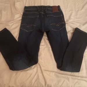 Replay Hyperflex mörkblå jeans - Mörkblå Replay Hyperflex jeans med klassiska kontrastsömmar och snygga detaljer på bakfickorna. Stretchigt material för extra komfort och passform. Märkespatch i läder baktill och Replay-logga på fickan framtill. Perfekta för en avslappnad och trendig look.