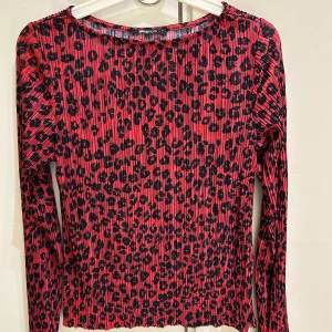 Röd leopardmönstrad topp Gina Tricot - Säljer en röd långärmad topp från Gina Tricot med svart leopardmönster. Toppen har plisserad struktur och rund halsringning. Materialet känns lätt och stretchigt, perfekt för dig som gillar att sticka ut med coola mönster och färger.