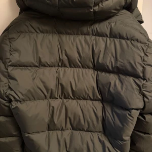 Mörkgrön dunjacka från J.Lindeberg - Säljer en mörkgrön dunjacka från J.Lindeberg med snyggt quiltad design och huva. Jackan har dragkedja framtill, två sidofickor och logga på bröstet. Perfekt för kalla dagar och riktigt chill stil.