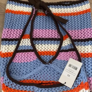 Randig virkad kortklänning XS - Färgglad virkad kortklänning med halterneck och knyt i nacken. Klänningen har breda ränder i blått, lila, vitt, orange och brunt. Perfekt för varma dagar och har en luftig, stickad känsla.