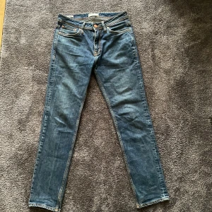 Mörkblåa jeans från Jack & Jones - Säljer ett par klassiska mörkblå jeans från Jack & Jones med fem fickor och snygga kontrastsömmar. Jeansen har normal midja och raka ben med en regular passform. Perfekta för dig som gillar en stilren och enkel look.