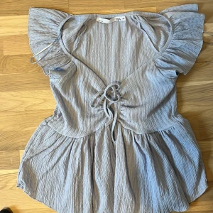 Ljusblå kortklänning från 157 - Supersöt ljusblå kortklänning från 157 med volangärmar och snygg snörning framtill. Klänningen har en crinklad struktur och v-ringning, vilket ger en chill och trendig vibe. Perfekt för varma dagar när du vill känna dig både bekväm och stylish.