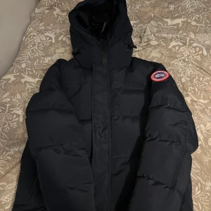 Mörkblå pufferjacka från Canada Goose - Beskrivning: Säljer min Canada Goose vinterjacka i mörkblått. Jackan är varm, bekväm och perfekt för kalla vintrar. Använd sparsamt och i mycket bra skick – inga skador, fläckar eller slitna delar. Har knappt använt den 