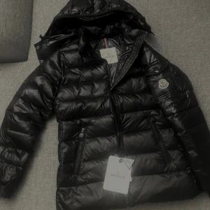 Svart Moncler pufferjacka med huva - Förnyar annons! Snygg svart pufferjacka från Moncler med matt finish, huva och dragkedja framtill i modell bady. Perfekt för kalla dagar och riktigt stilren look. Scann, nfc och taggar finns. Priset kan diskuteras vid snabb affär! 