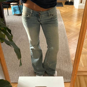 Bootcut jeans från Jane Norman - Ljusblå bootcut jeans från Jane Norman med låg midja och klassiska fem fickor. Snygga slitningar framtill, dubbla knappar i midjan och broderad logga på insidan. Jeansen har en lätt utsvängd passform och är tillverkade i bomull med en skön jeanskänsla.