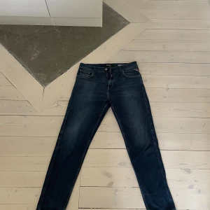 Replay blå jeans SANDOT tapered fit - Snygga blå jeans från Replay i modellen SANDOT med tapered fit. Jeansen har klassisk femficksdesign, Replay-lapp bak i skinnimitation och diskreta slitningar. Tillverkade i bomull med en mörk tvätt och kontrastsömmar. Perfekta för en avslappnad och trendig look.