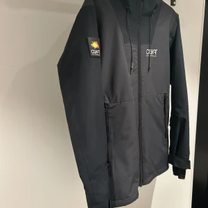 Svart vinterjacka från CLWR - Svart vinterjacka från CLWR Colourwear med huva och snörning. Jackan har dragkedja framtill, två fickor med dragkedja och logotyp på bröstet samt ärmen. Storlek small. Köpt för 1500 ny. Pris kan diskuteras!