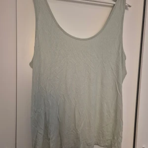 Ljusgrön ribbad topp från xlnt - En ljusgrön, ärmlös ribbad topp från xlnt i storlek 3XL. Toppen har en enkel och avslappnad passform med rundad halsringning. Tillverkad i mjuk och stretchig mix av modal och polyester, perfekt för varma dagar. 