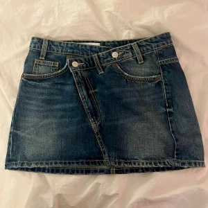 Mörkblå jeanskjol med sned knäppning - Snygg mörkblå jeanskjol från Zara med cool sned knäppning framtill. Klassiska fickor både fram och bak. Perfekt för dig som gillar denim och vill ha en trendig twist på din outfit.❣️