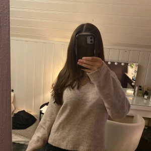 Beige stickad v-ringad tröja - Mysig beige stickad tröja med v-ringning och långa ärmar. Tröjan har en enkel och stilren design med ribbade muddar vid ärmslut och nederkant. Perfekt för lager-på-lager och chill dagar.