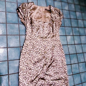 Kortklänning från Tiger of Sweden - Supersöt kortklänning i beige med småblommigt mönster och lätt puffade korta ärmar. Klänningen har en fyrkantig ringning och figurnära passform. Perfekt för dig som gillar romantiska och feminina detaljer.