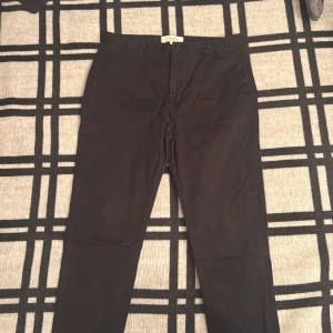 Svarta chinos från Legends, storlek L - Snygga svarta chinos från Legends i storlek L. Klassisk rak passform med knappstängning fram, bälteshällor och två fickor bak med knapp. Perfekta för en clean och stilren look. Materialet känns mjukt och har en lätt stretch för extra komfort.