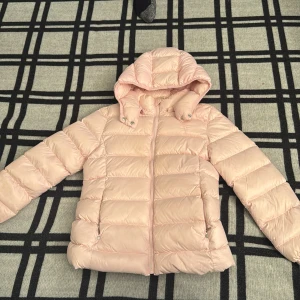 Ljusrosa pufferjacka från Polo Ralph Lauren - Säljer en ljusrosa pufferjacka från Polo Ralph Lauren med huva och dragkedja framtill. Jackan har quiltad design och långa ärmar, perfekt för kyliga dagar. Materialet är syntet och jackan har en clean, modern look som är enkel att matcha.