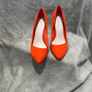 Röda mockapumps från Bianco - Snygga röda pumps från Bianco i mjuk mocka med spetsig tå och hög klack. Skorna har en klassisk siluett och en intensiv färg som verkligen sticker ut. Perfekta för dig som vill ha en statement-sko med elegant vibe.