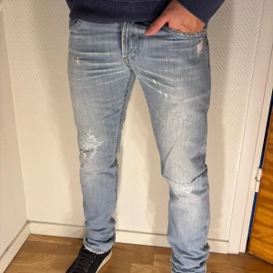 Dondup jeans  - Säljer ett par ljusblå jeans med slitningar och trasiga detaljer både fram och bak. Jeansen har raka ben, klassiska fem fickor och en avslappnad vibe. Perfekta för dig som gillar en streetstyle-look med lite edge.